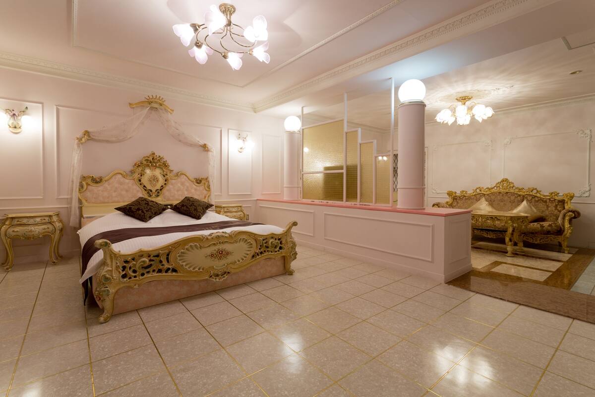 A luxurious bedroom with a large ornate bed, a vanity with a mirror, and a chaise lounge.