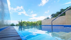 A clear blue swimming pool with a wooden deck, surrounded by a concrete wall and a metal railing. - Cuna Hotel (El Nido)
