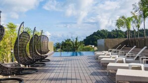 A wooden deck with lounge chairs and wicker chairs, overlooking a swimming pool. - Cuna Hotel (El Nido)