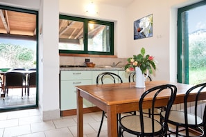 A kitchen with a wooden table and chairs, a window with a view of greenery, and a vase with flowers on the table.