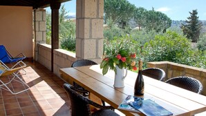 A patio with a wooden table, wicker chairs, a blue lounge chair, and a vase with flowers. - Il Borgo Centro Vacanze (Guardistallo)