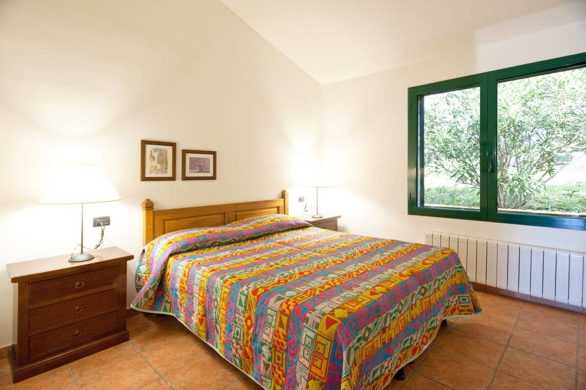 Ein Schlafzimmer mit Bett, Nachttisch, Kommode, einem Fenster mit Aussicht und zwei gerahmten Bildern an der Wand.