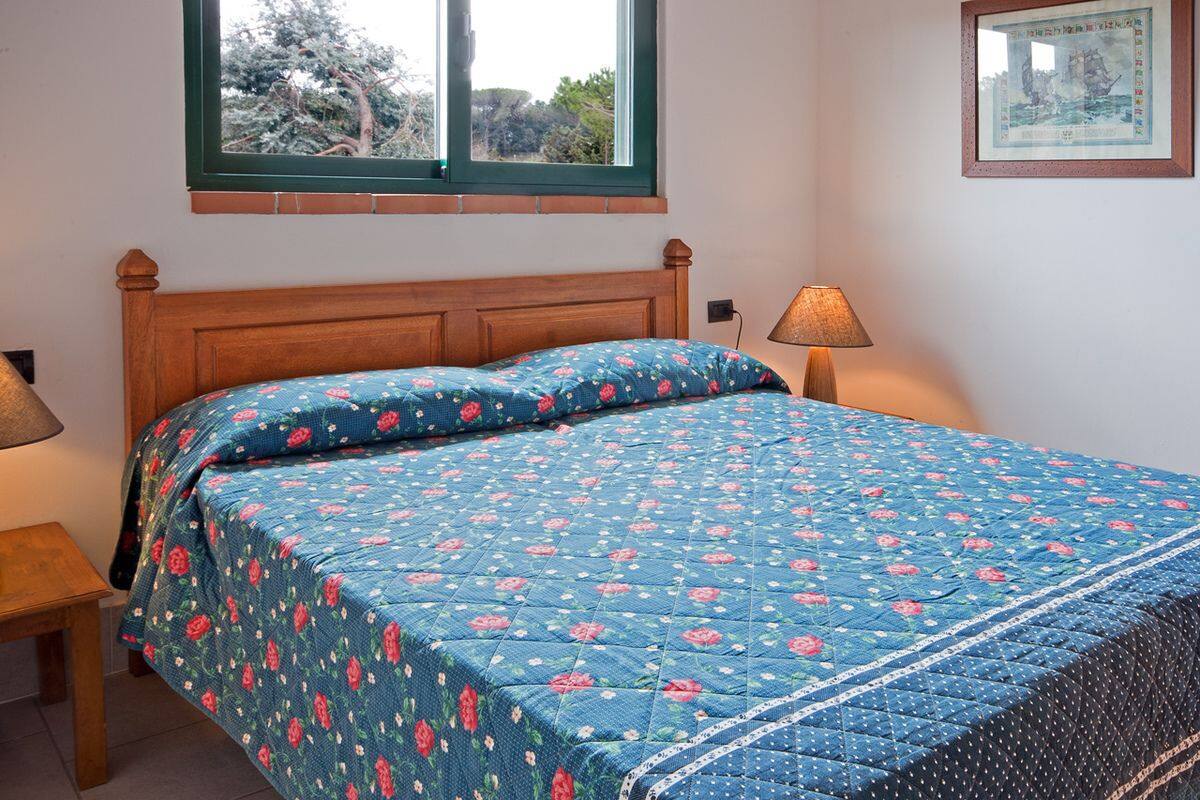 Ein Schlafzimmer mit einem Holz-Kopfteil, einer blumigen Bettdecke, zwei Nachttischlampen und einem gerahmten Bild an der Wand.