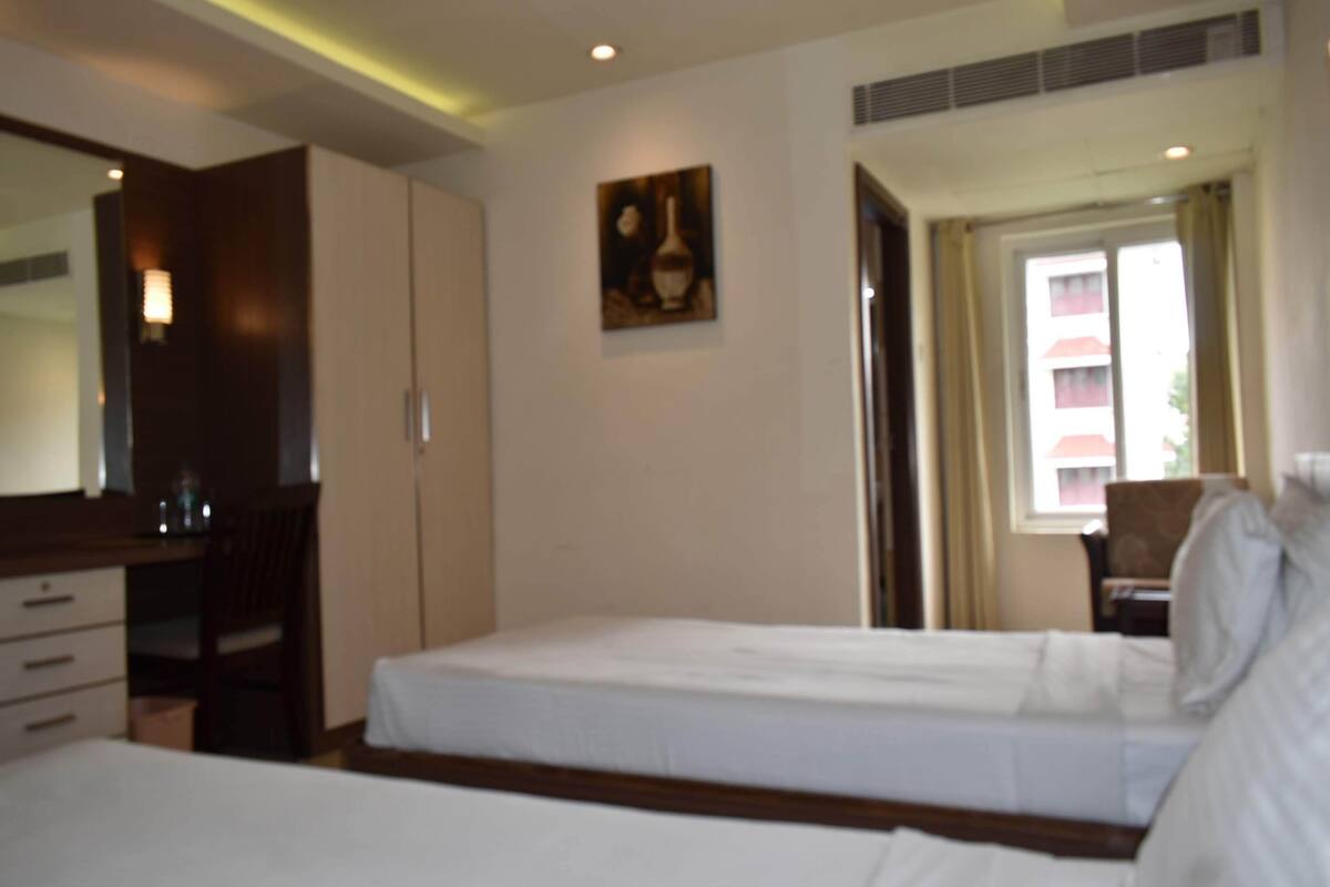 A hotel room with two beds, a desk, a chair, a wardrobe, and a painting on the wall.