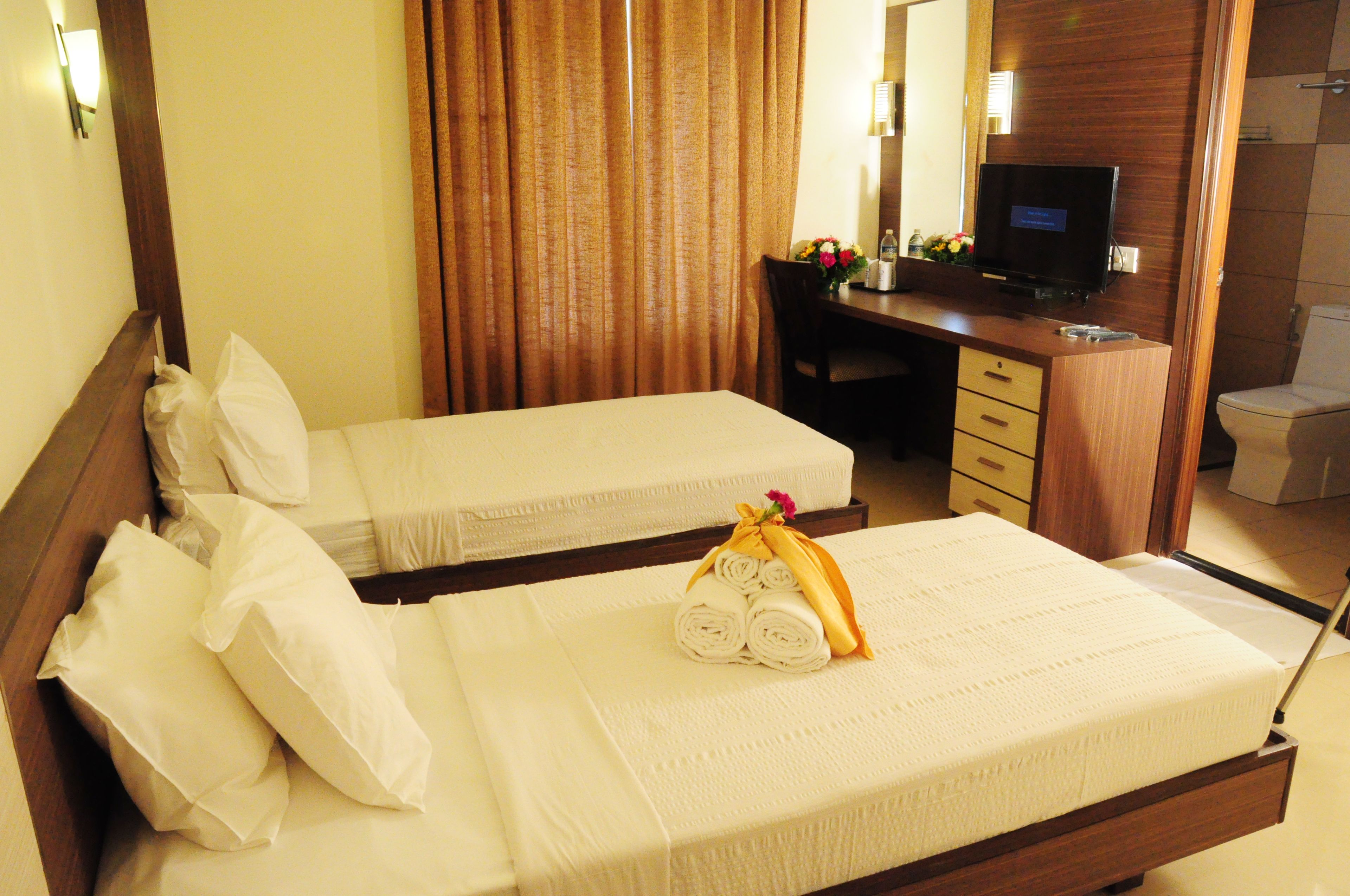 A hotel room with two single beds, a desk with a computer, and a bathroom.