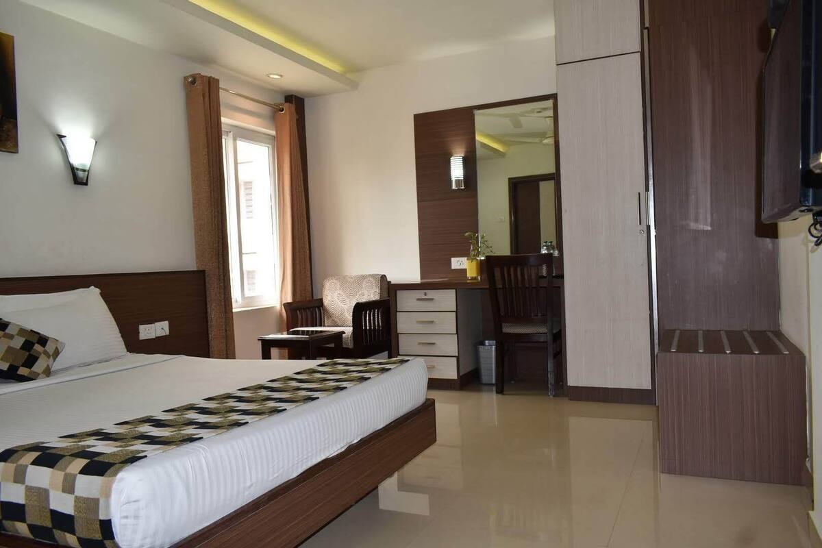 A hotel room with a large bed, a desk, a chair, a wardrobe, and a mirror.