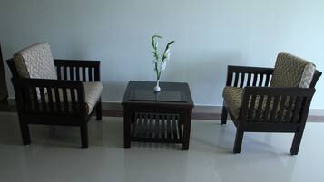 Two dark wooden chairs with patterned cushions, a small square table with a vase of white flowers, and a plain wall in the background.