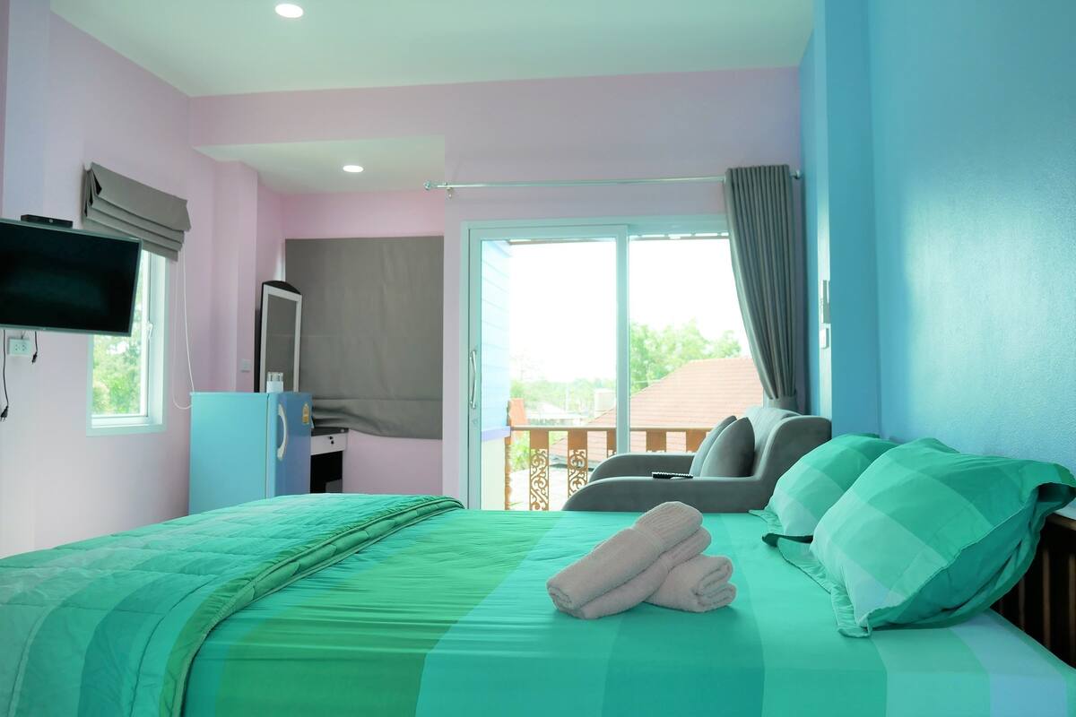 A bedroom with a bed, a TV, a desk, and a balcony view.