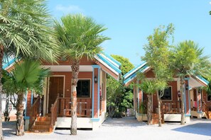 A row of small, two-story buildings with a red and blue color scheme, surrounded by palm trees and other greenery. - Sansook Resort (Tha Mai)