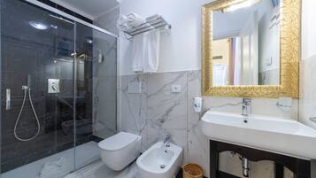 A modern bathroom with a glass-enclosed shower, a bidet, a sink, and a mirror with a gold frame.