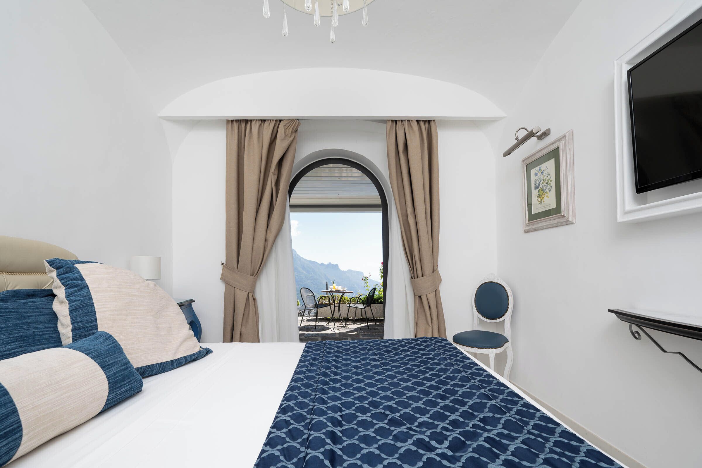 Une chambre à coucher avec un lit, une chaise, un téléviseur et une vue sur l’extérieur.
