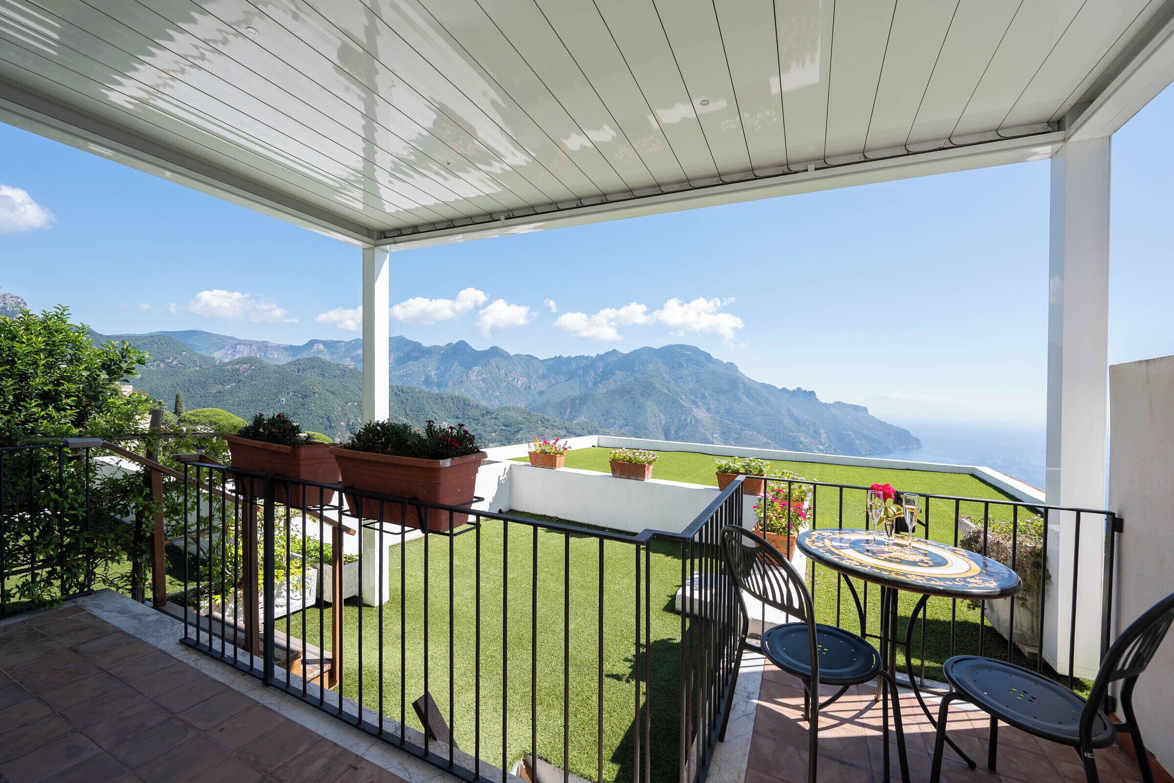 A balcony with a view of mountains, a table with chairs, and potted plants.