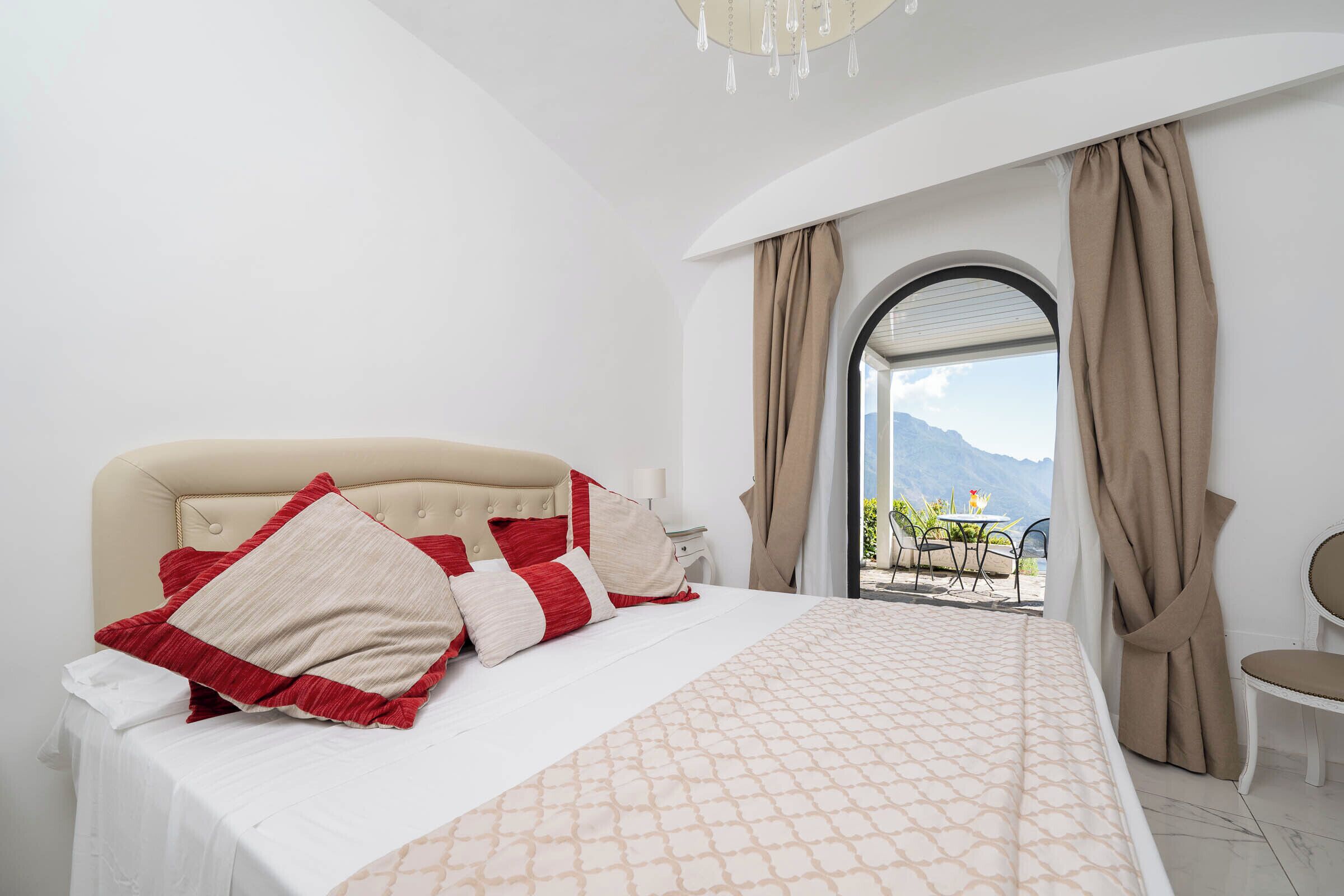 A hotel room with a bed, a chair, a table, and a view of mountains through a window.