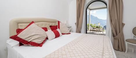 A hotel room with a bed, a chair, a table, and a view of mountains through a window.