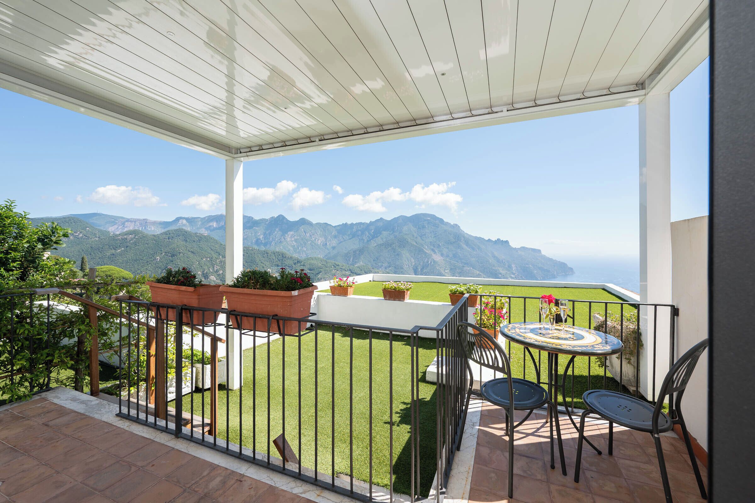 Un balcone con vista sulle montagne, un tavolo con sedie e piante in vaso.