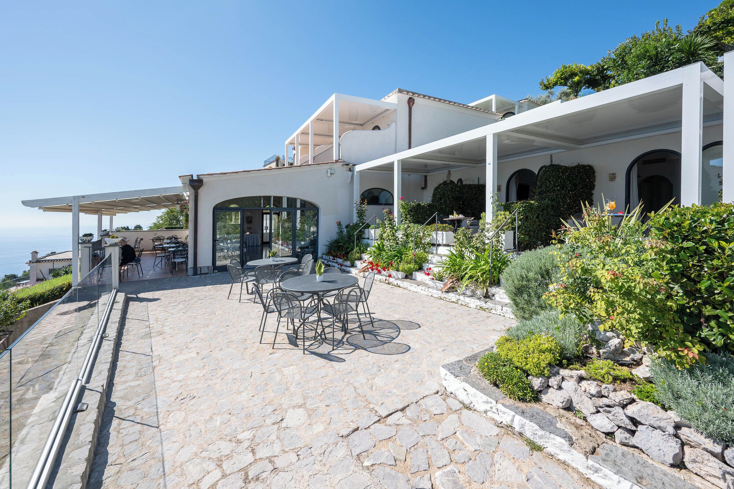 A modern outdoor patio with stone flooring, outdoor seating, and a view of the sea.