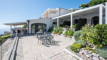 A modern outdoor patio with stone flooring, outdoor seating, and a view of the sea.