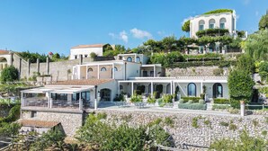 A hillside property with multiple buildings, including a large villa with a green roof and a smaller structure with a red roof. - Villa Amore (Ravello)