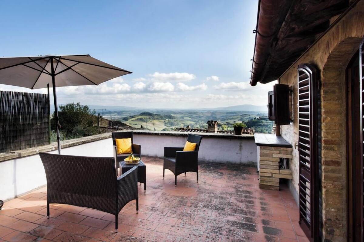 Een terras met rieten stoelen en een parasol, met uitzicht op een prachtig landschap.