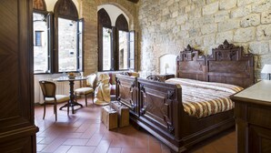 Quarto tradicional com uma cama grande, uma escrivaninha de madeira e uma parede de pedra.