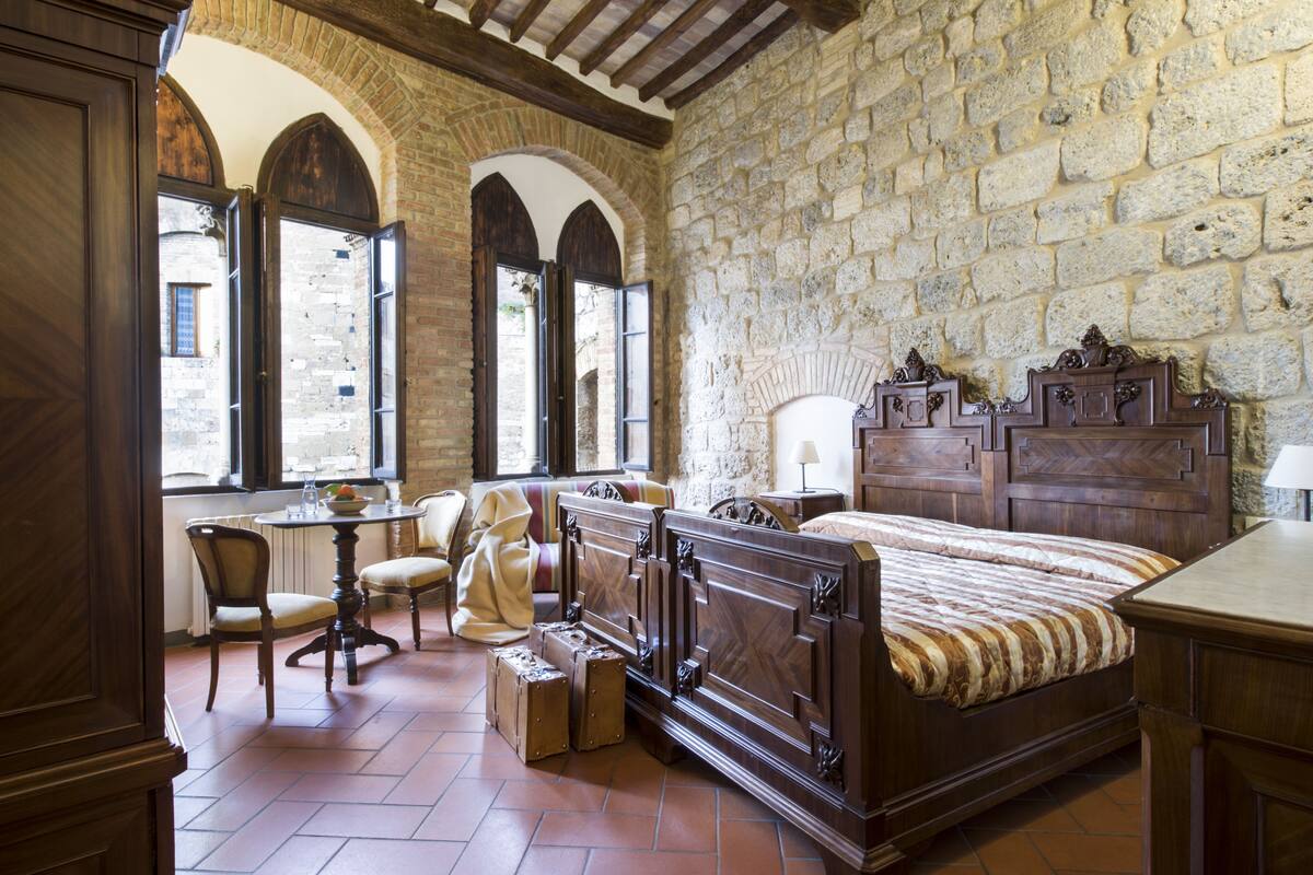 Een klassieke kamer met een groot bed, een houten bureau en een stenen muur.
