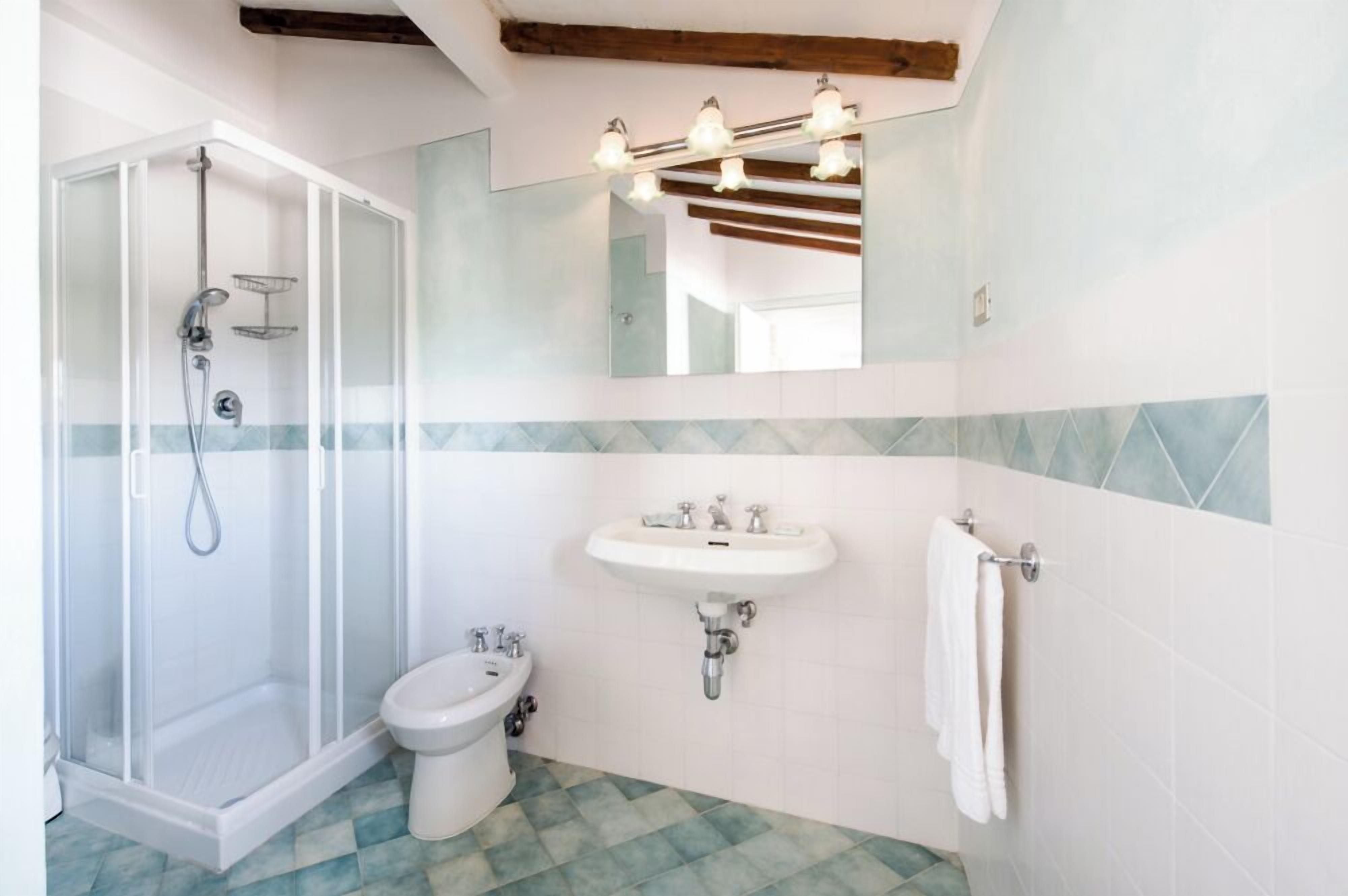 A bathroom with a glass-enclosed shower, a pedestal sink, and a toilet.