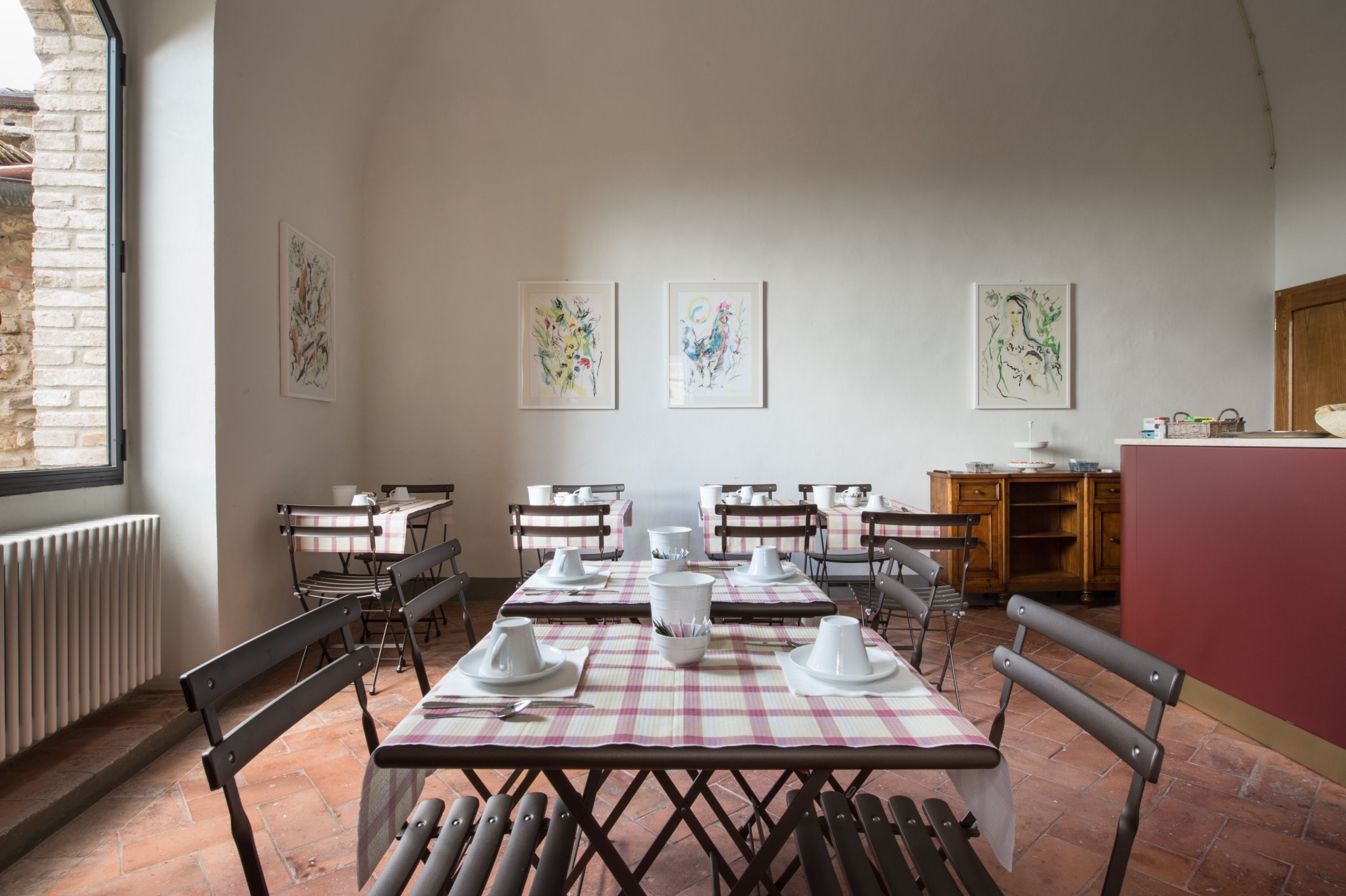 A dining area with tables set for four, chairs, and artwork on the walls.