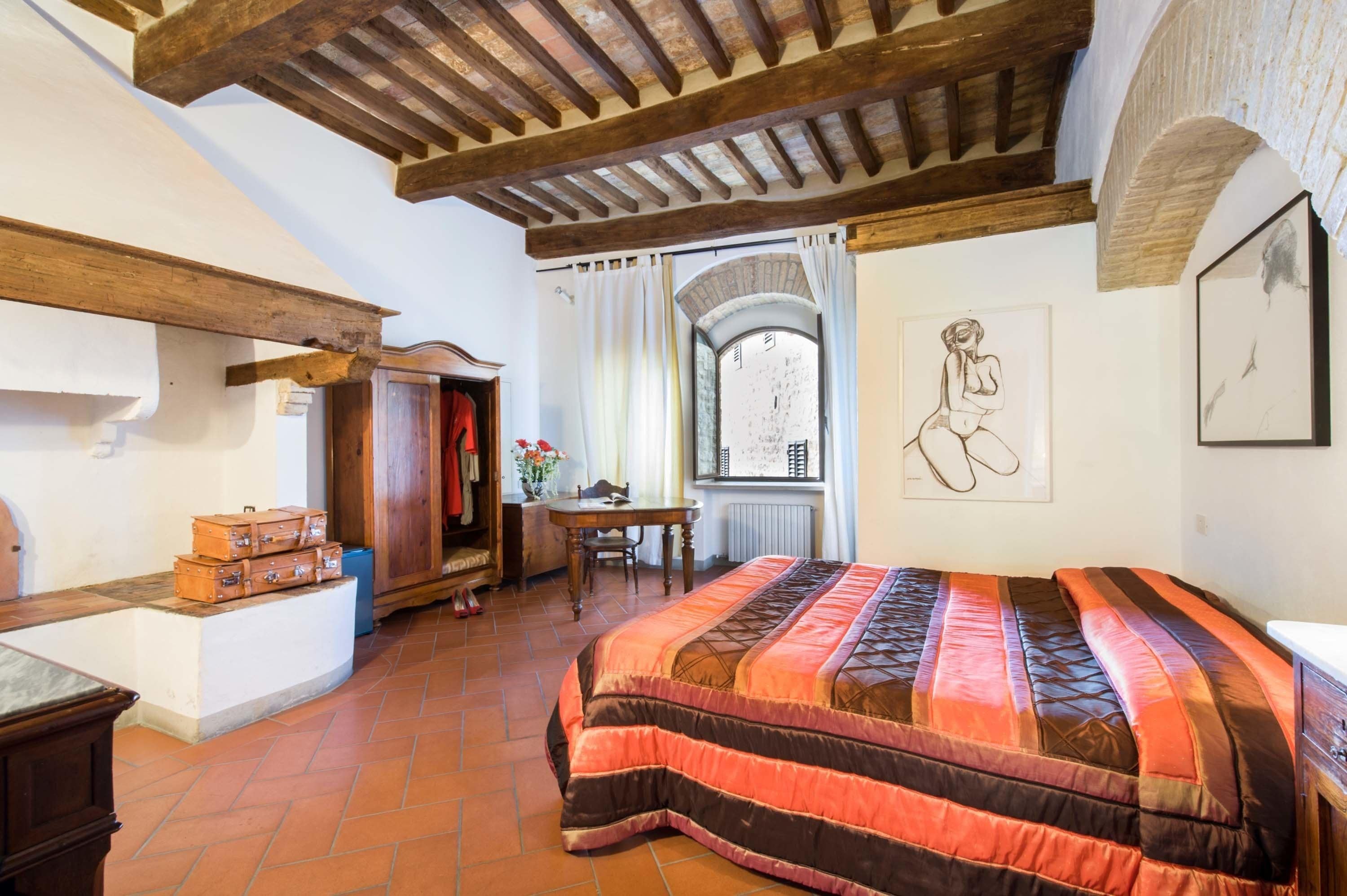 A bedroom with a large bed, wooden beams, a desk, and a window with a view.