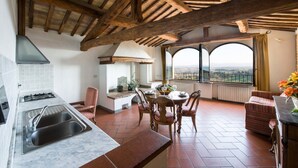 Uma cozinha com uma ilha grande, uma área de refeições com mesa e cadeiras, e vista através de janelas arqueadas.