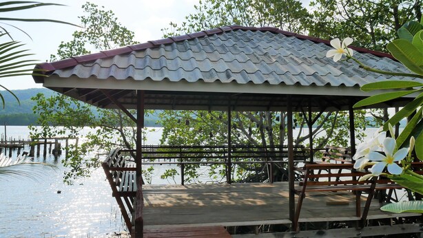 Un pavillon en bois, surmonté d’un toit de tuiles, surplombe un plan d’eau paisible, le tout étant entouré d’une végétation luxuriante.