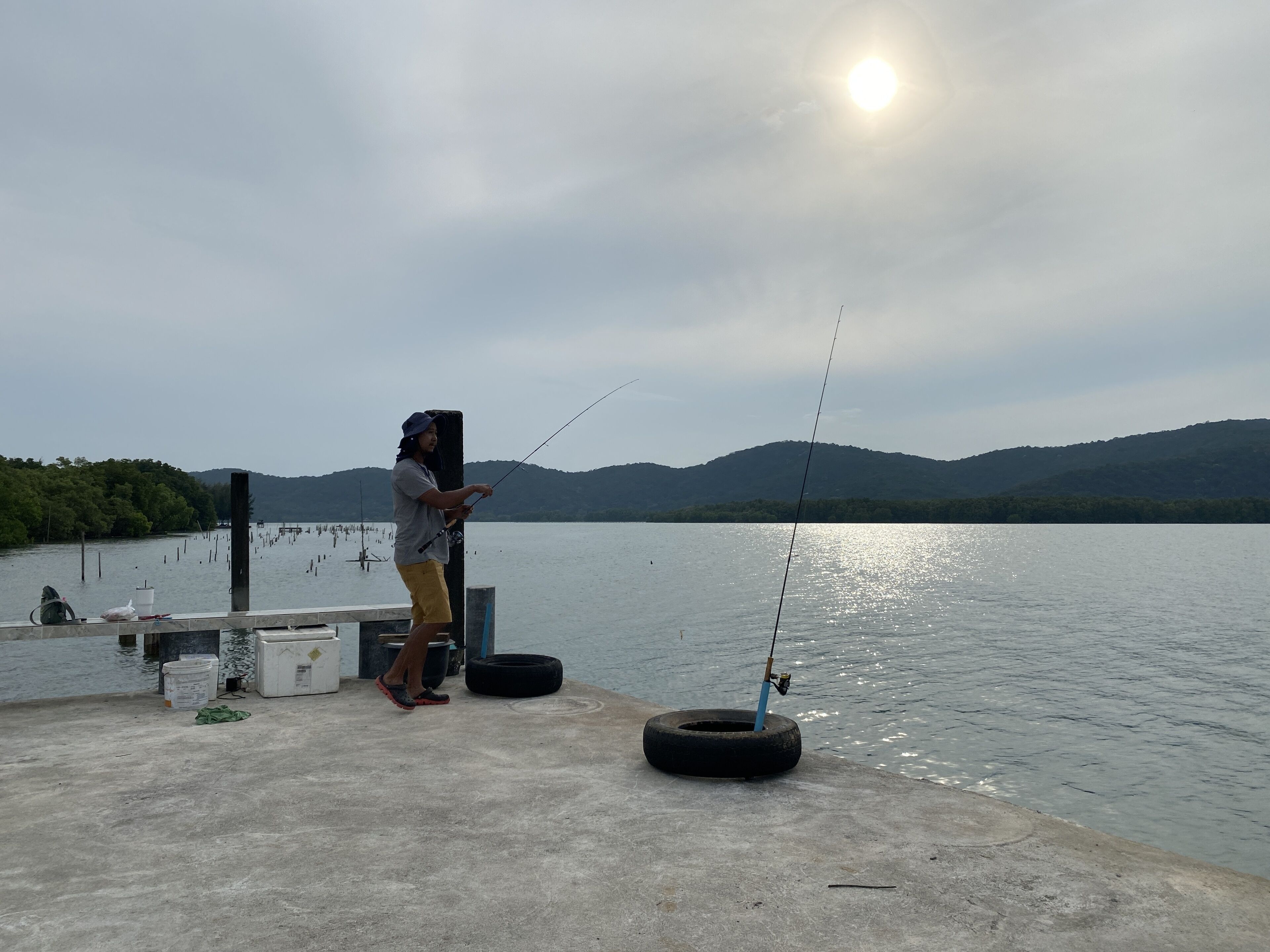 A person fishing by a calm lake with a clear sky and distant hills.