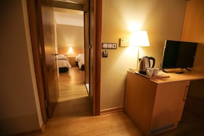 Une chambre d’hôtel avec un bureau en bois, une télévision, une lampe et un lit recouvert de draps blancs.