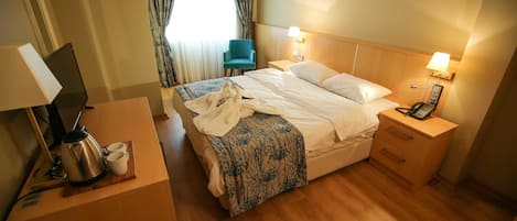 Una habitación de hotel con cama, mesitas de noche, un escritorio con lámpara, una silla y una ventana con cortinas.