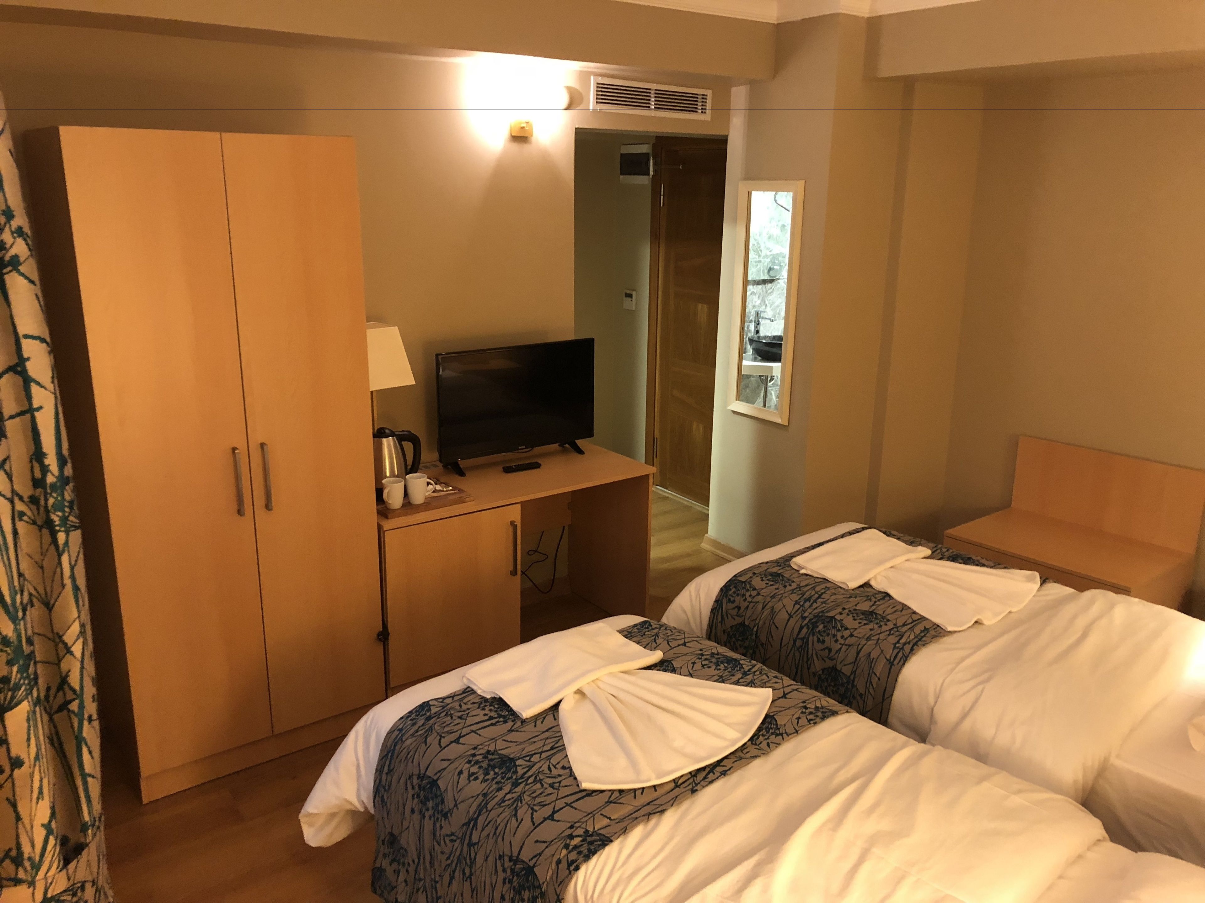 A hotel room with two beds, a television, a desk with a lamp, and a wardrobe.