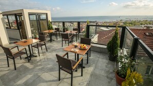 A terrace with tables and chairs, potted plants, and a view of the sea and cityscape. - Artika Hotel (Istanbul)