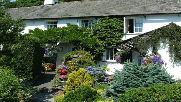 Un bâtiment blanc doté d’un toit en pente, entouré d’une végétation luxuriante et de plantes en fleurs.