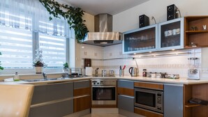 Una cocina moderna con electrodomésticos de acero inoxidable, horno empotrado y microondas. Hay una ventana con cortinas translúcidas y una orquídea en maceta sobre la encimera.