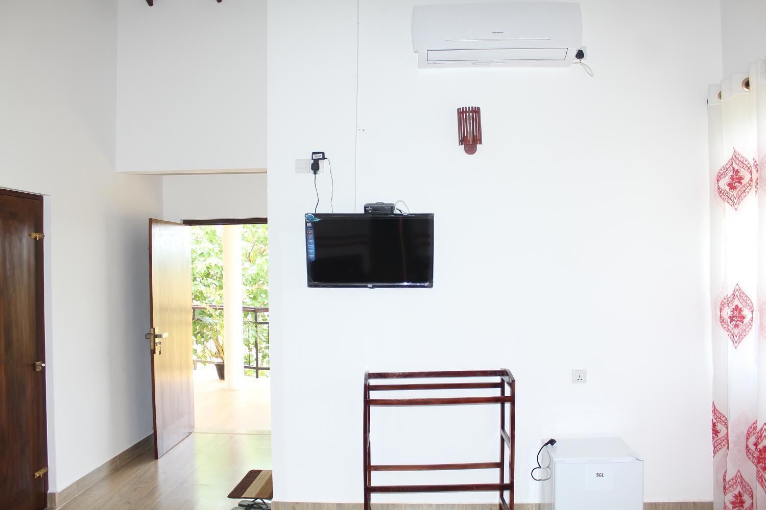 Een kamer met een aan de muur bevestigde televisie, een klein wit apparaat en een houten rek.