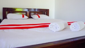 A neatly made bed with white linens and red accents, a wooden headboard, and two rolled towels on the bed. - Lavender Home Rest (Thissamaharama)