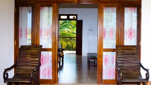 A room with two wooden chairs, a small table, and a view of a tropical garden through a glass door. - Lavender Home Rest (Thissamaharama)