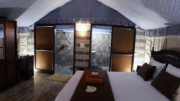 A bedroom with a large bed, a wooden wardrobe, a desk, and a sliding glass door leading to a bathroom. - Ecoterra Solace Resort (Narendranagar)