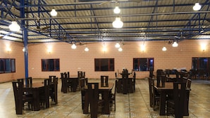 A spacious indoor area with multiple tables and chairs arranged for dining. - Ecoterra Solace Resort (Narendranagar)