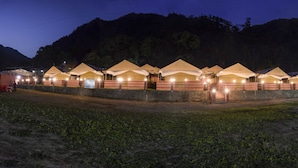 A row of tents with a brick wall and a mountain in the background. - Ecoterra Solace Resort (Narendranagar)