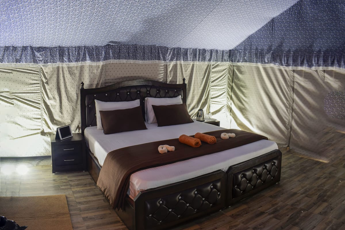 A spacious tent-style room with a large bed, a bedside table, and a view of the tent's interior.