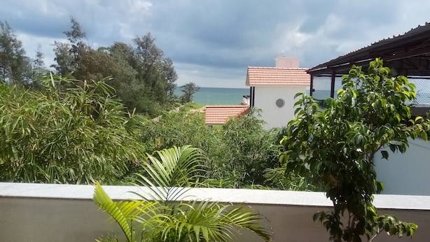 A rooftop terrace with lush greenery, a view of the sea, and a building with a red-tiled roof. - Meya Beach Walk Hotel (Tirukalukundram)