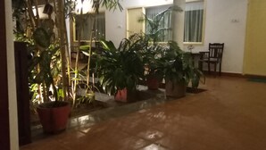 A spacious room with a tiled floor, several potted plants, a wooden chair, and a yellow door. - Meya Beach Walk Hotel (Tirukalukundram)
