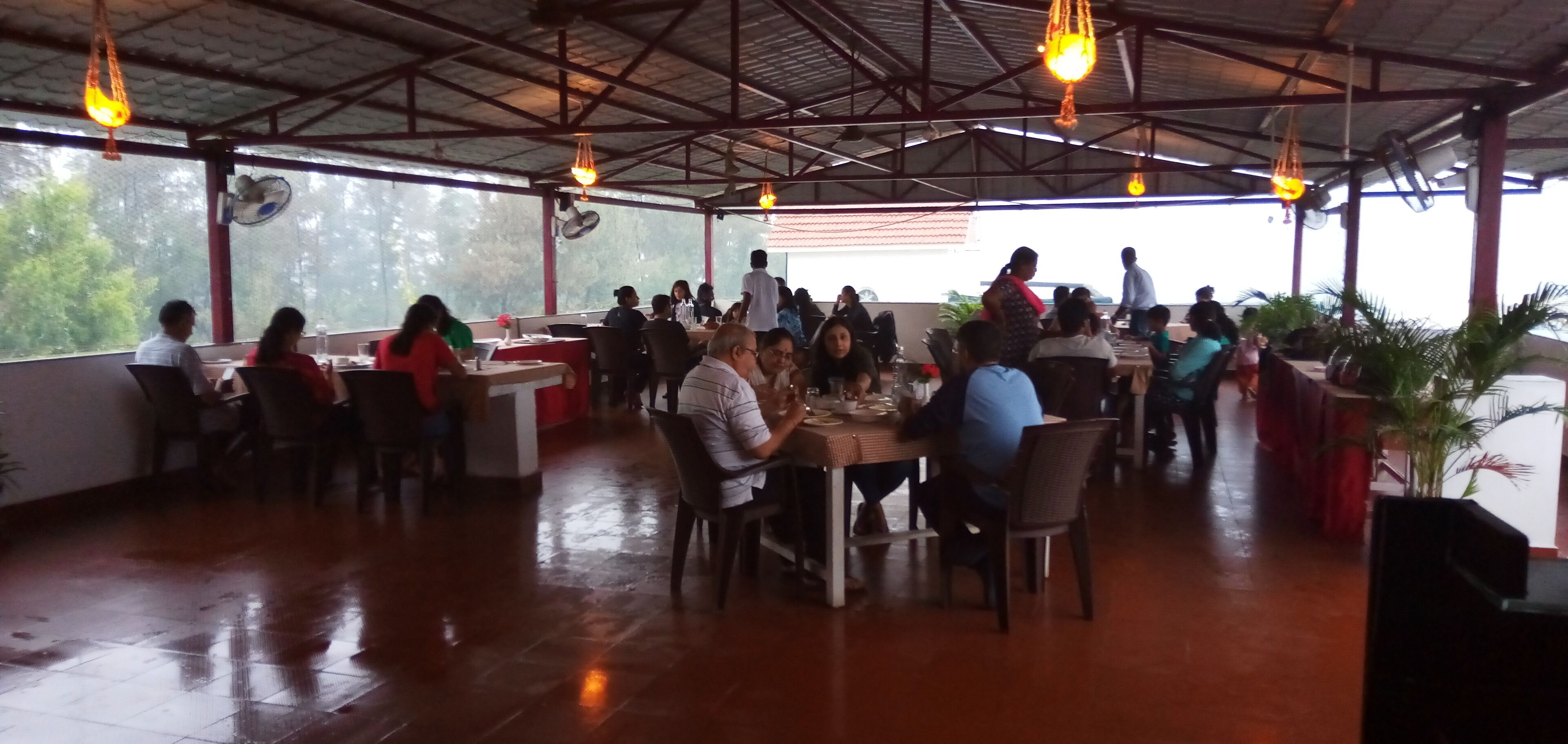 A spacious indoor dining area with multiple tables and chairs, large windows, and hanging lights.