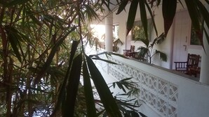 A covered outdoor area with a white railing, potted plants, and wooden furniture. - Meya Beach Walk Hotel (Tirukalukundram)
