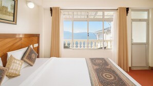A hotel room with a large bed, a view of mountains, a balcony, and a painting on the wall. - Hotel White Yak (Darjeeling)