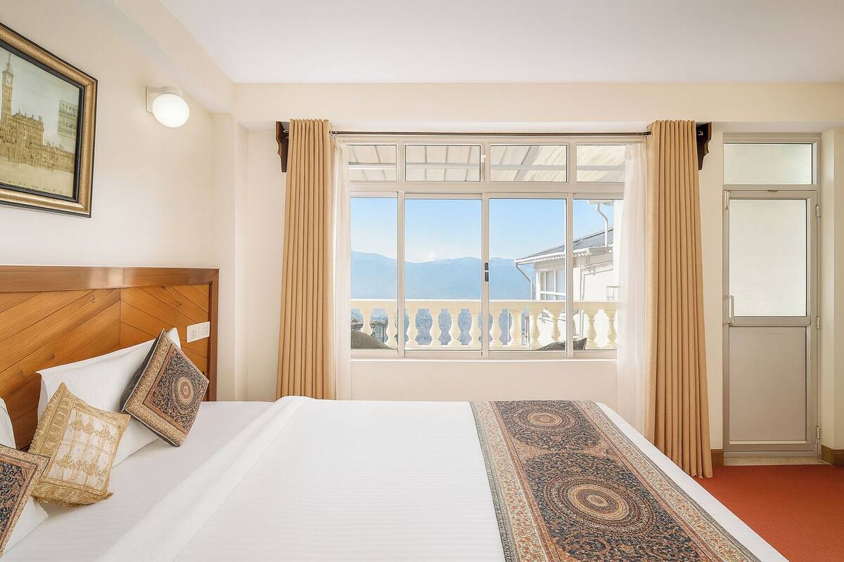 Habitación de hotel con una cama grande, vistas a las montañas, un balcón y un cuadro en la pared.